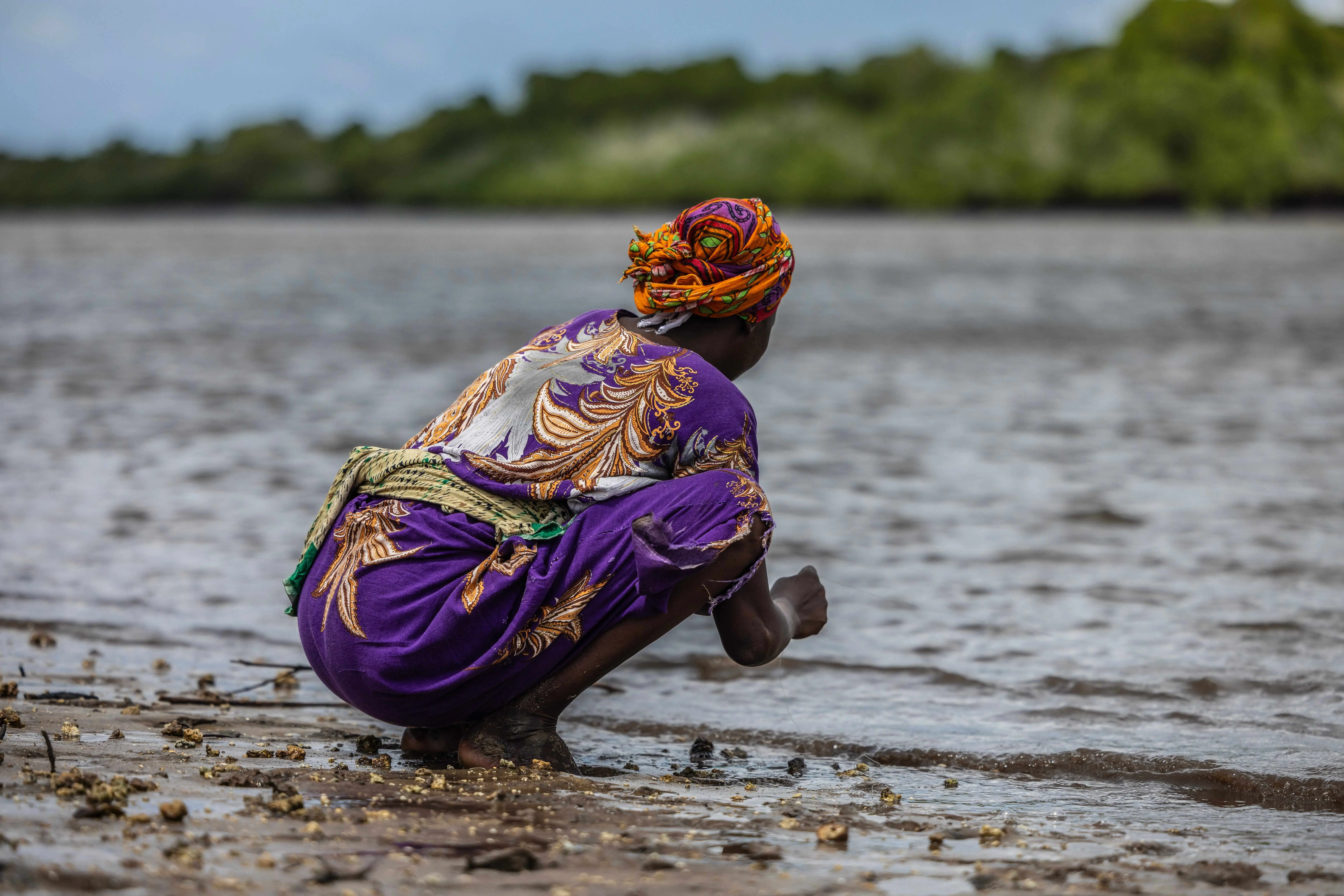 A woman crouching down searching in the water